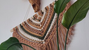 A macrame wall hanging with a cow skull and cow horns decoration, a macrame blanket, and a large green plant.