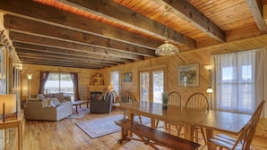Una cabaña de madera espaciosa con una gran mesa de comedor, varias sillas, un sofá y una chimenea.