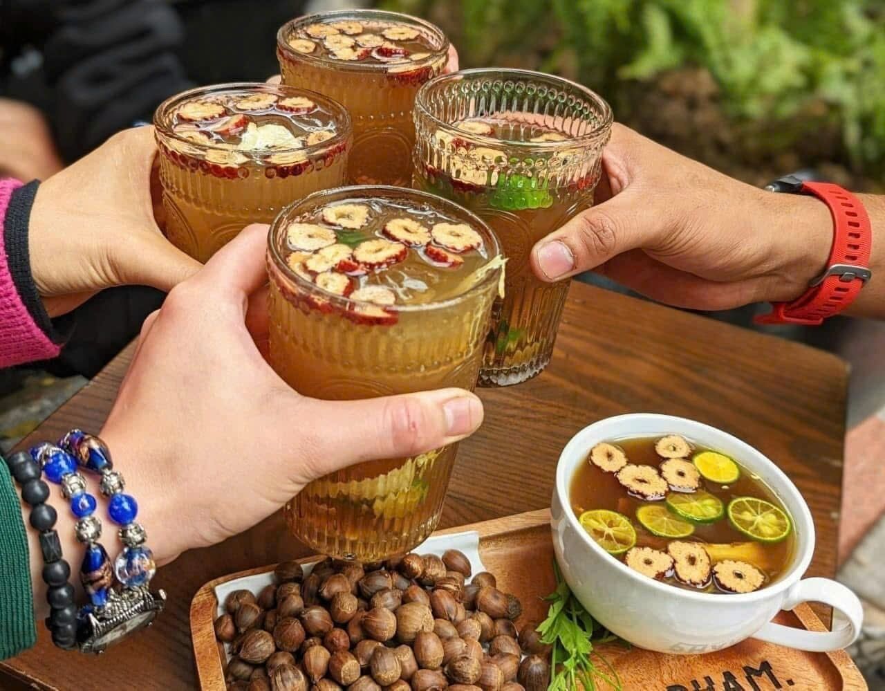 Un groupe de personnes trinque avec des verres remplis d’une boisson agrémentée de noix et de tranches de fruits. On peut également apercevoir sur la table un bol de noix et une tasse de thé avec des tranches de fruits.