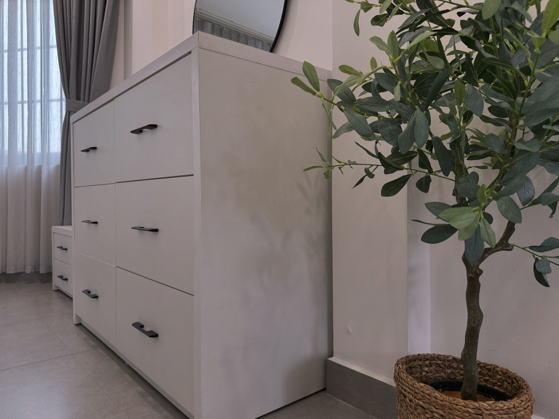 A white wardrobe with multiple drawers and a small potted plant beside it.