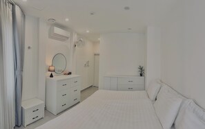 Un dormitorio con cama, mesita de noche, cómoda, espejo, equipo de aire acondicionado y una planta en maceta.