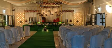 A wedding venue with a green carpet aisle, white chairs, and floral decorations.