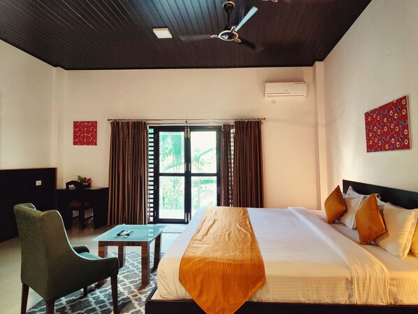 A hotel room with a bed, a desk, a chair, and a ceiling fan. - THE YELLOW BAMBOO RESORT AND SPA (Virajpet)