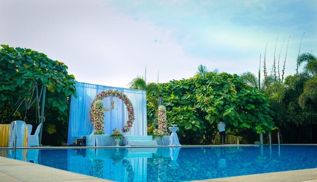 Un área de piscina con una estructura azul decorada con arreglos florales, rodeada de abundante vegetación.