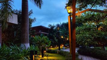 A well-lit garden pathway with a lamp post, surrounded by lush greenery and a paved walkway.