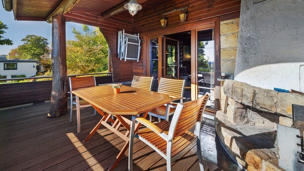 A wooden deck with a table and chairs, a stone fireplace, and a view of the surrounding area. - Holiday Home 'Ferienhaus Bad Gandersheim' with Private Terrace, Private Garden and Wi-Fi (Bad Gandersheim)