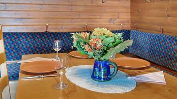 Uma mesa de madeira com um vaso azul de flores, uma taça de vinho e pratos.