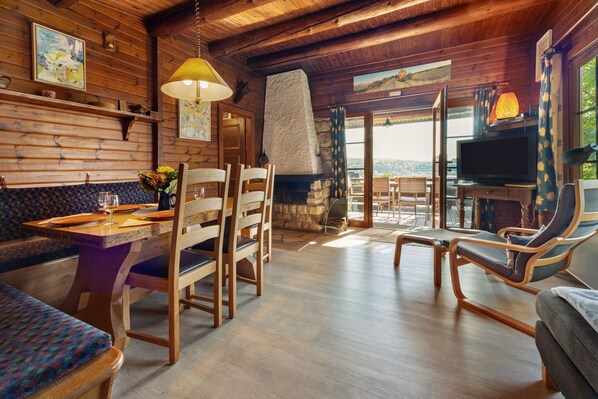 A wooden interior with a dining area, seating, a fireplace, and a television.