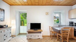 Eine Küche mit Fernseher, Holzstühlen, einem weißen Schrank und einem Fenster.