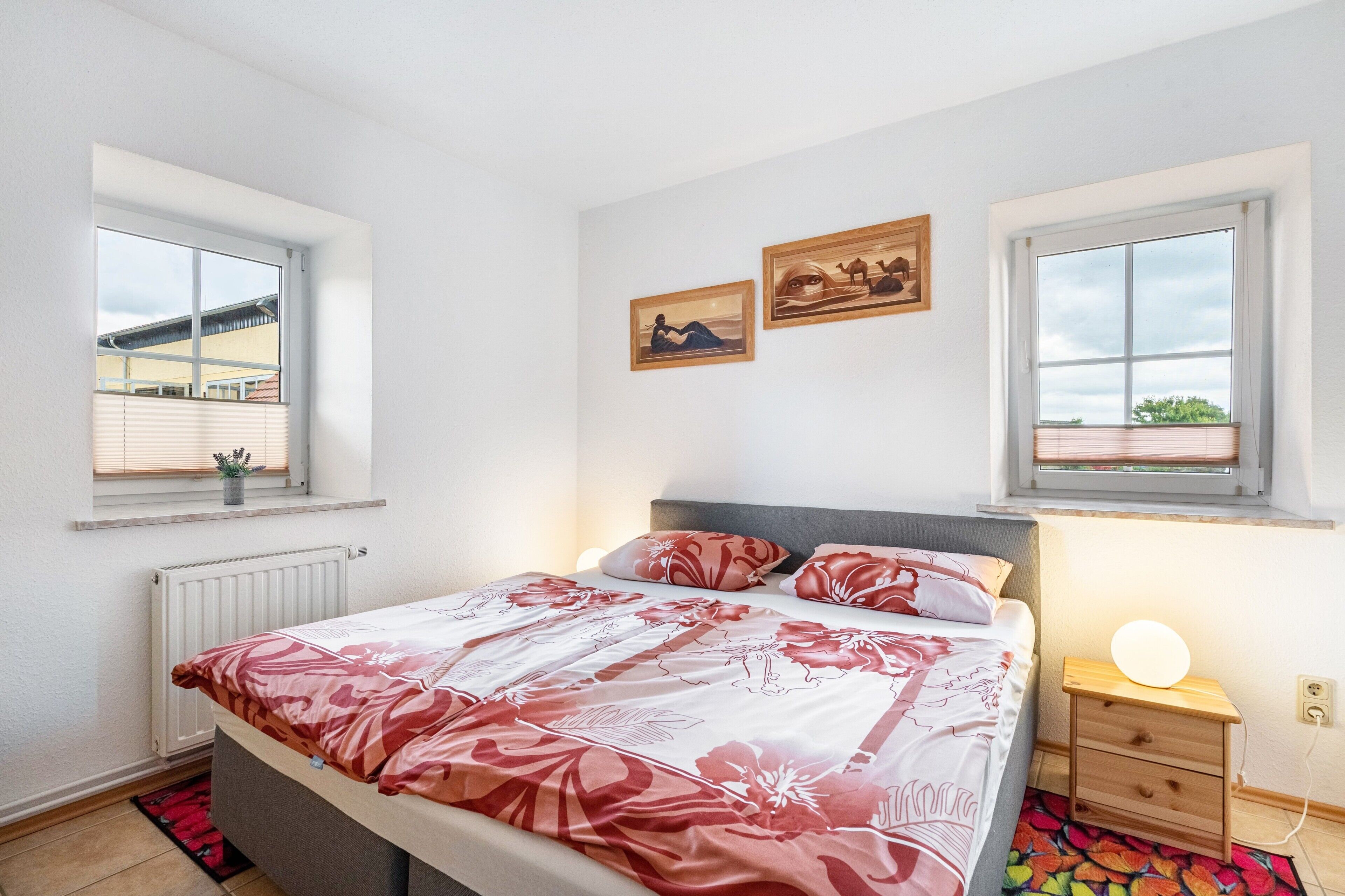 Una camera da letto con un letto, due finestre, un comodino con una lampada e un'opera d'arte appesa al muro.