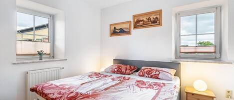 Una camera da letto con un letto, due finestre, un comodino con una lampada e un'opera d'arte appesa al muro.