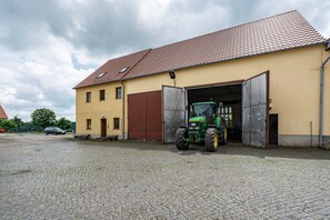 A building with a red-tiled roof, a green tractor parked in front, and a cobblestone ground.