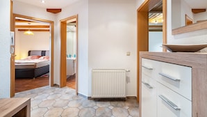 Un pasillo con techo de madera, un radiador, una cama y un baño con espejo y lavamanos.