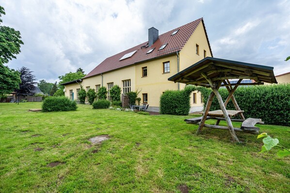 A house with a red-tiled roof, a covered outdoor seating area, and a well-maintained lawn.