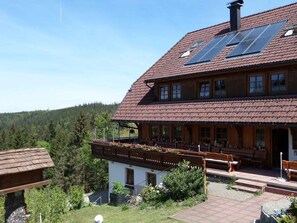 Una casa a due piani in legno, con tetto inclinato, pannelli solari e un balcone con sedute.