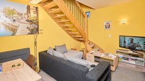 A living room with a sofa, a coffee table, a TV, a bookshelf, a painting, and a wooden staircase.