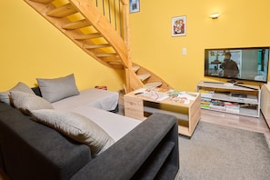 Olohuoneessa on sohva, kirjoja sisältävä sohvapöytä, televisio ja puinen portaikko.