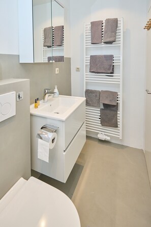 Une salle de bain moderne avec un lavabo blanc, un miroir, un porte-serviettes et des toilettes.