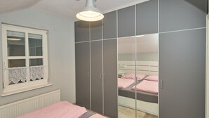 A bedroom with a bed, a wardrobe, a window with lace curtains, and a radiator.