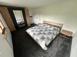 A bedroom with a bed, a wardrobe, a mirror, and a small bedside table.