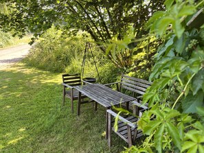 A wooden bench and table set in a grassy area with dense foliage in the background.