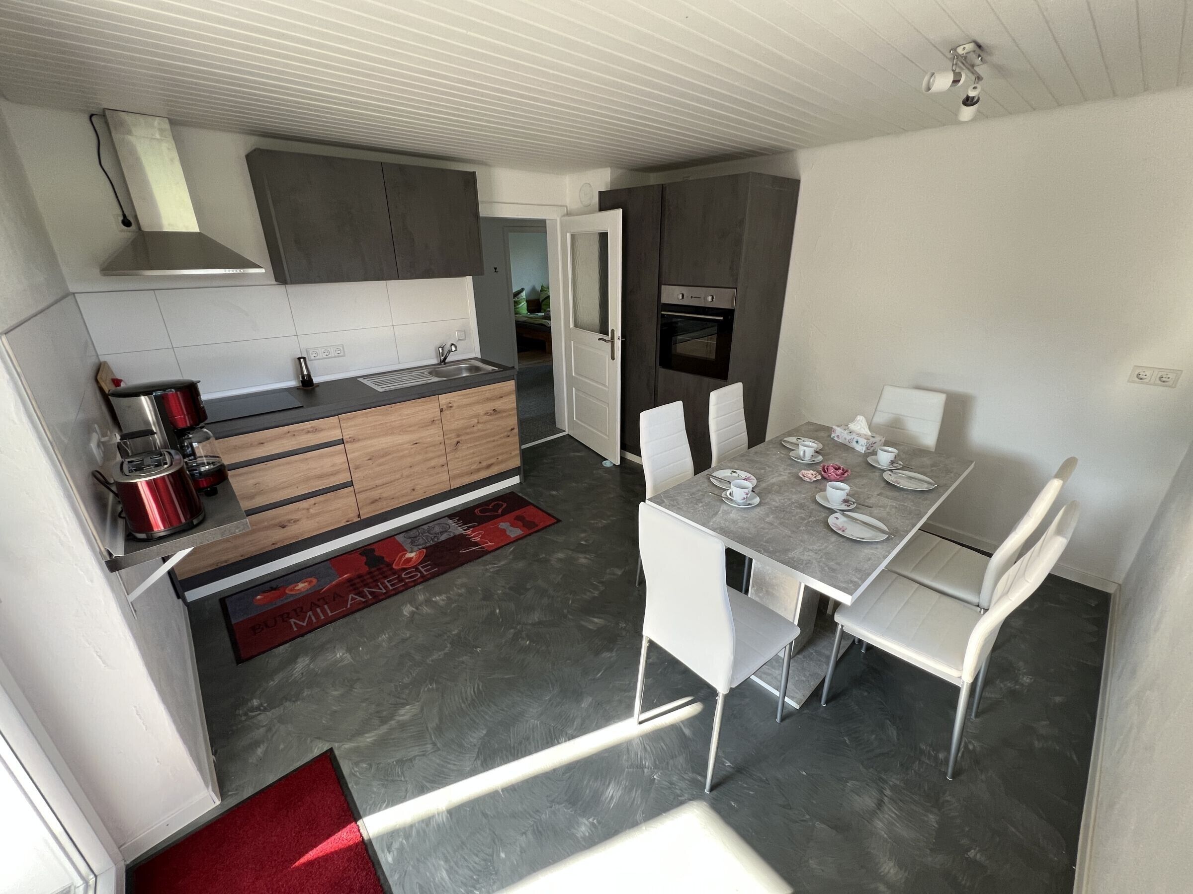 A modern kitchen with a built-in oven, a coffee maker, and a dining area with a table set for two.
