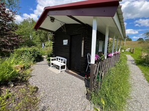 A rustic log cabin with a porch, a bench, and a gravel path leading to it.