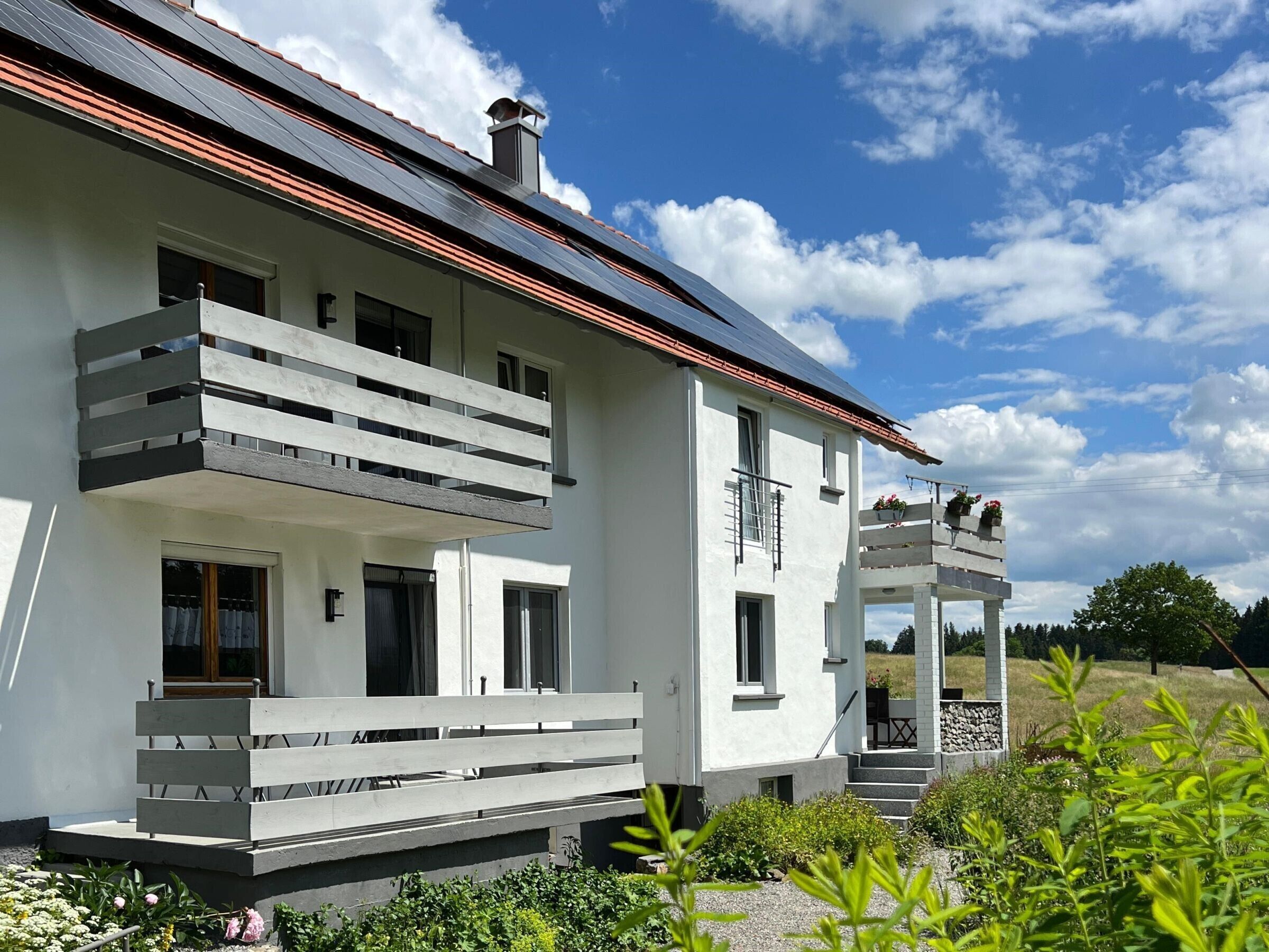 Ein modernes, zweistöckiges Haus mit Balkon, Schornstein und Garten.