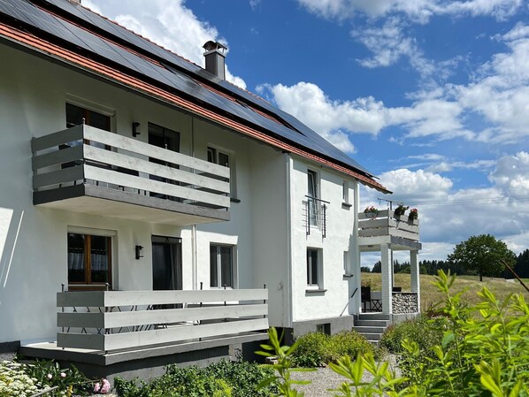 Una casa moderna de dos pisos con balcón, chimenea y jardín.