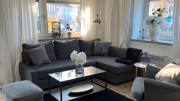 Un salon moderne avec un canapé gris, une table basse en verre et un tapis noir.