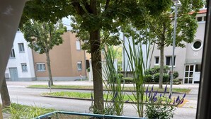 Un balcon avec une table et des chaises en bois, des plantes en pot et une vue sur la rue et les immeubles.