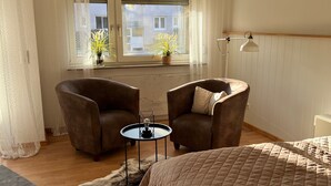 Une chambre à coucher avec un lit, deux fauteuils, une petite table, une fenêtre avec des rideaux et une lampe.