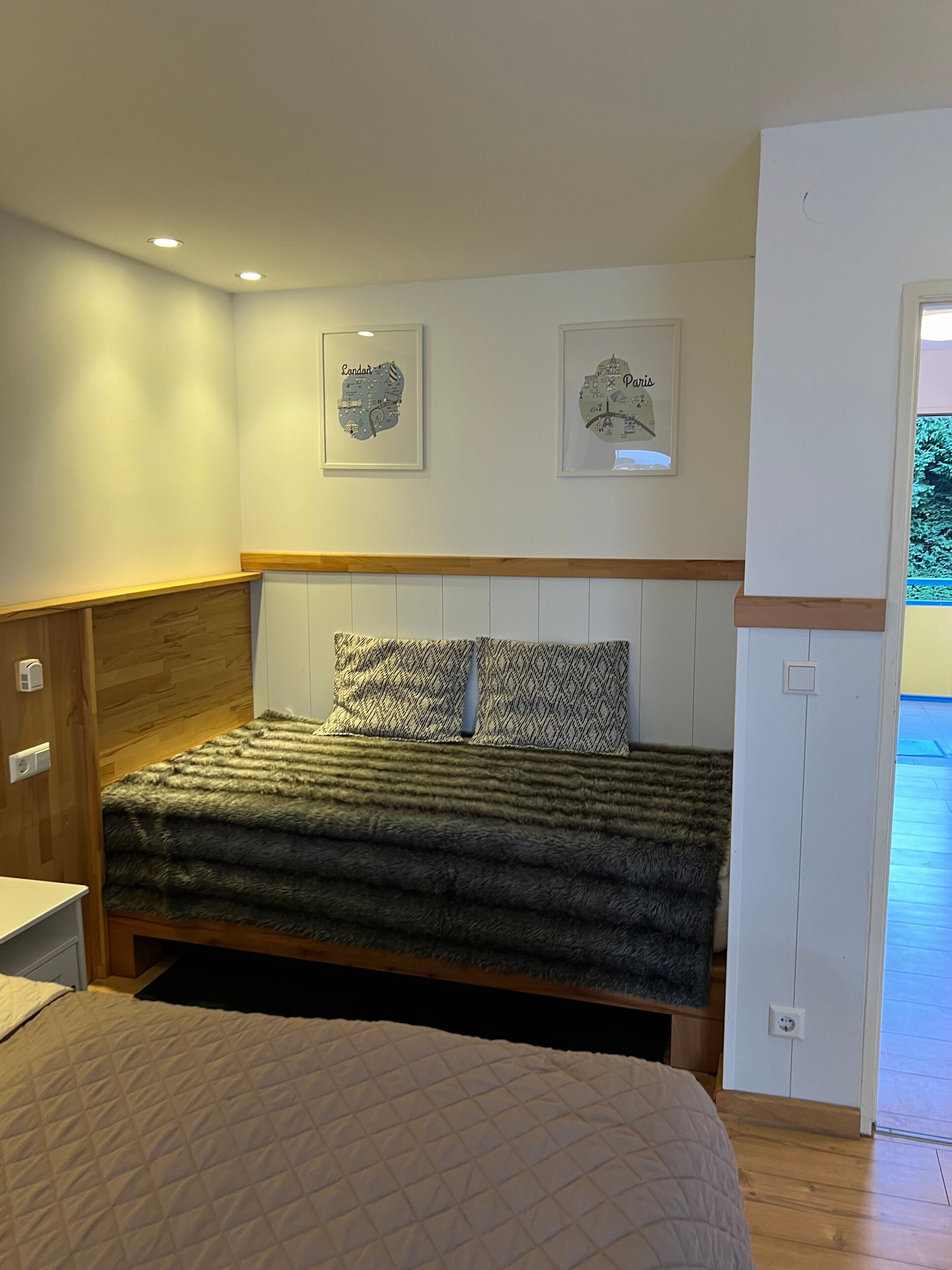 Un dormitorio con cama, cabecera de madera, dos cuadros en la pared y una puerta que da a un balcón.