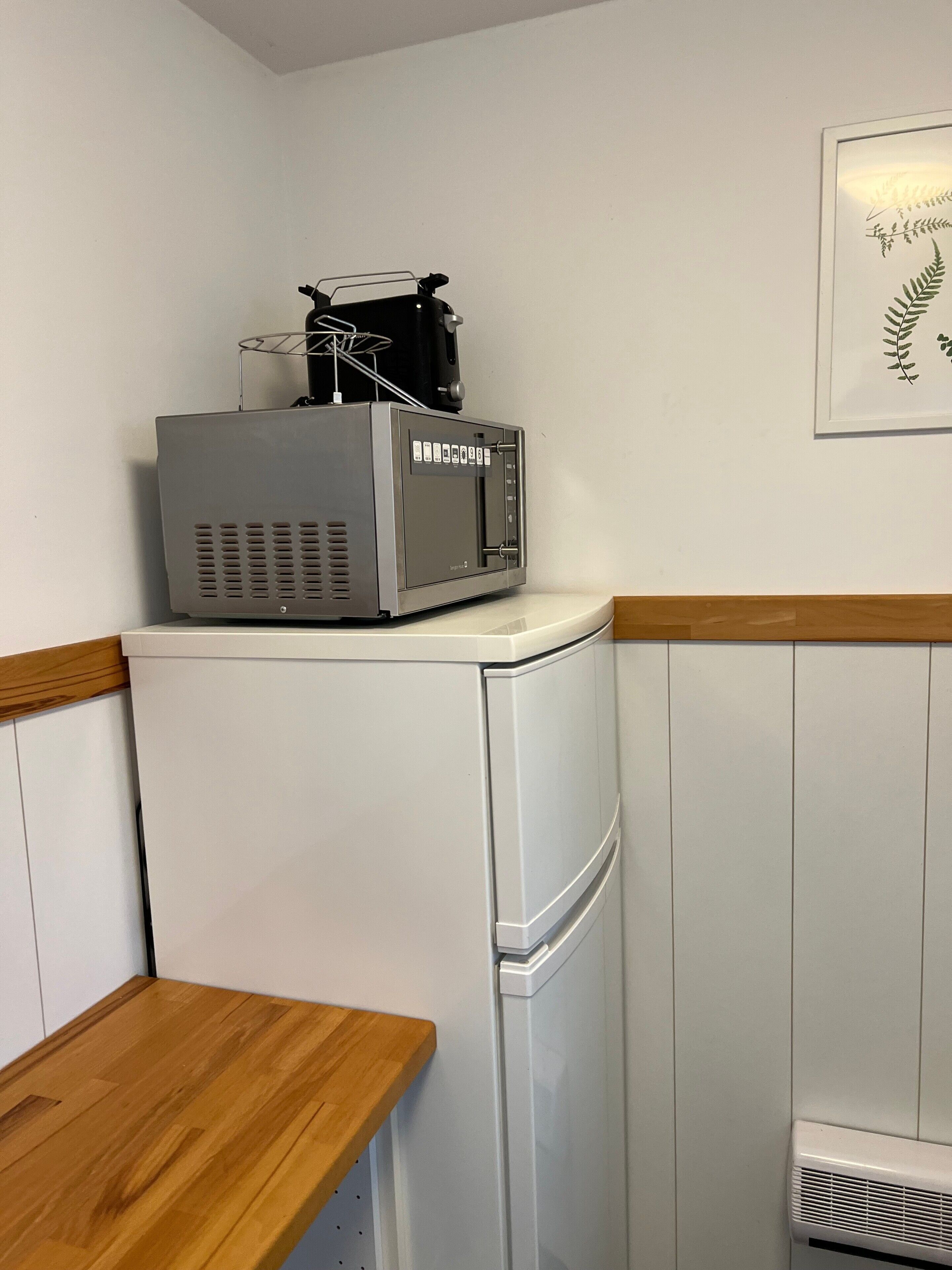 Une petite cuisine équipée comprenant un réfrigérateur, un four à micro-ondes et une petite table en bois.