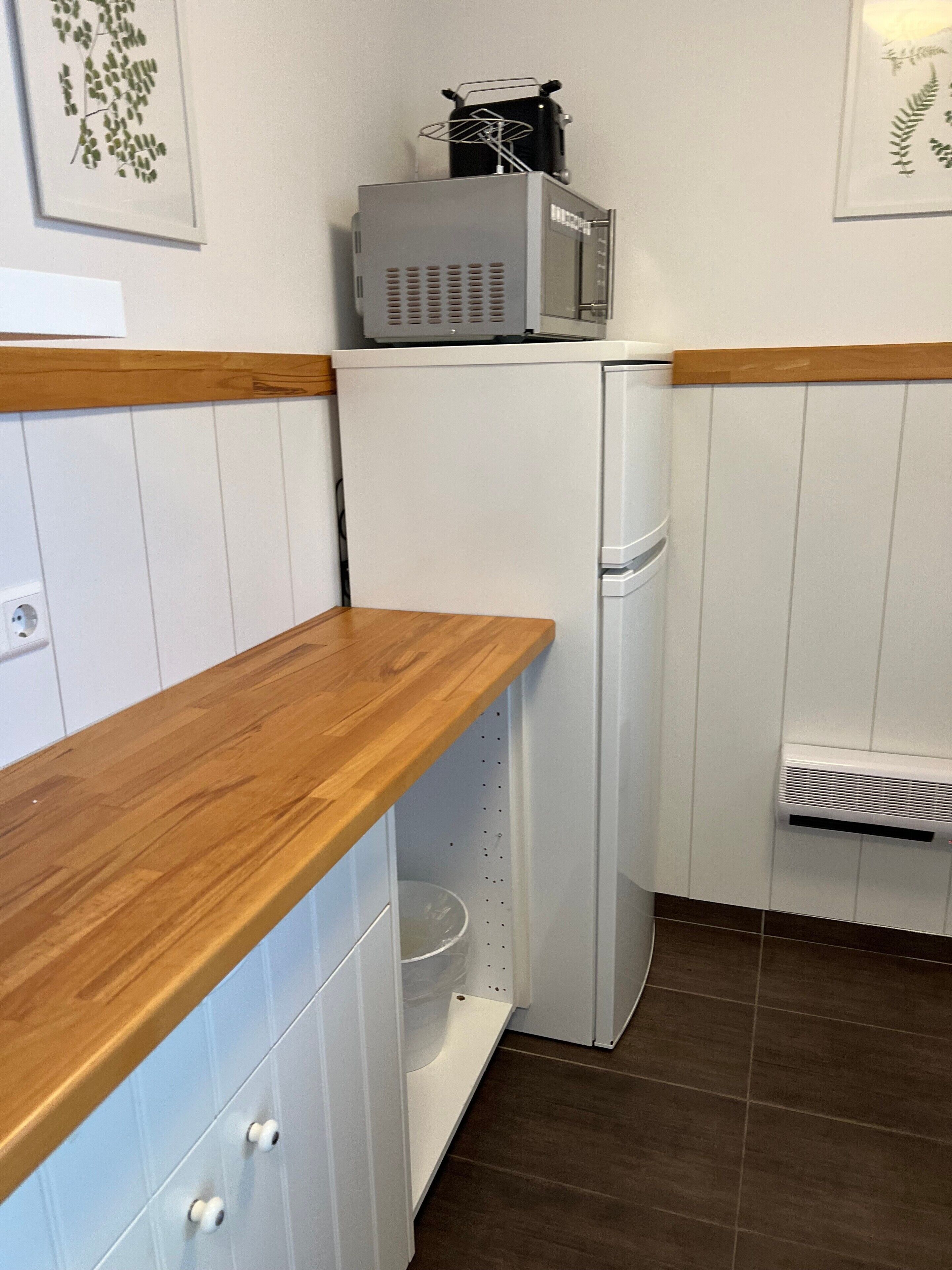 Een compacte keuken met een houten aanrecht, een witte koelkast en een wandairconditioner.
