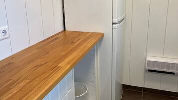 Een compacte keuken met een houten aanrecht, een witte koelkast en een wandairconditioner.