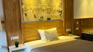 Een hotelkamer met een groot bed, houten paneelbekleding, een wandkunst van een druk station en een klein nachtkastje met een plant.