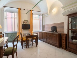 Une cuisine avec un coin repas, comprenant une table en bois, des chaises, un téléviseur fixé au mur et un meuble avec des portes en verre.