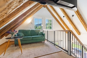 A loft bedroom with a green sofa, a small table, and a view of the outdoors. - Holiday Home 'Die Alte Mühle Am Hanselishof' with Mountain View, Private Terrace and Wi-Fi (Schenkenzell)