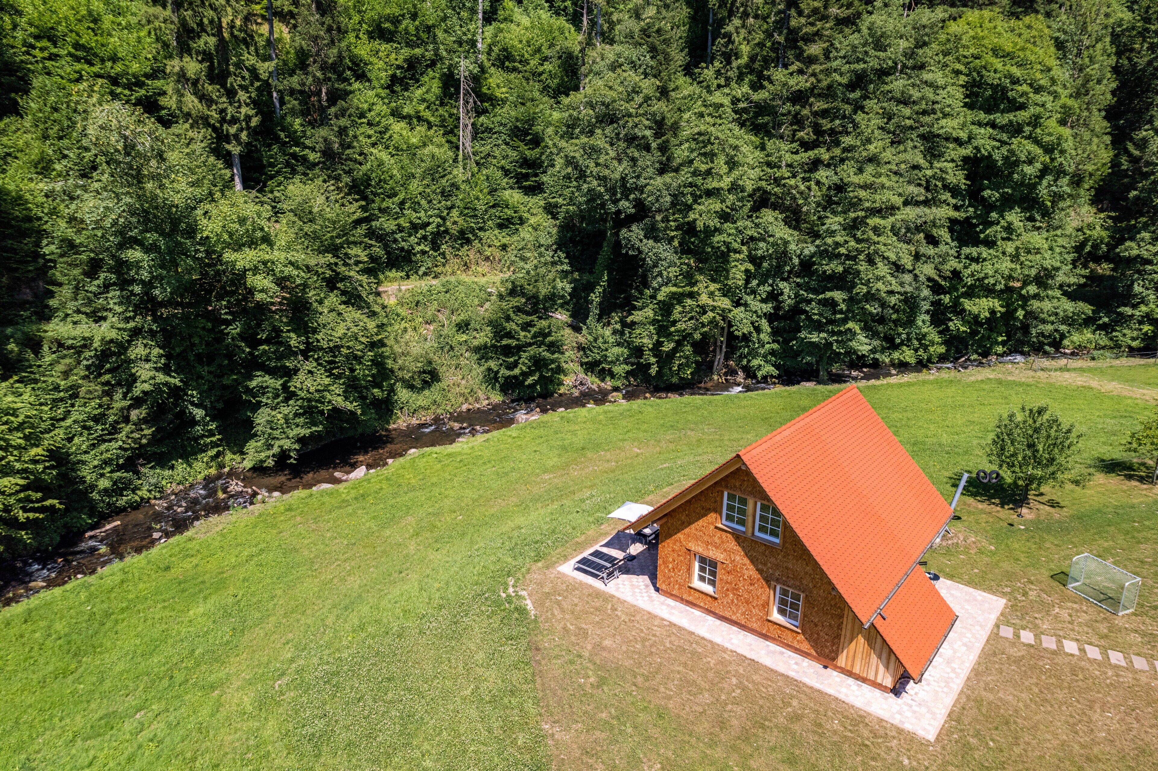 Una casa de un piso con techo inclinado, rodeada por un patio cubierto de césped y un bosque denso.