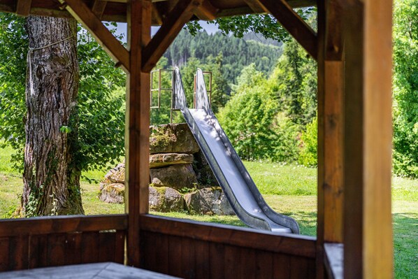 A wooden structure with a metal slide, surrounded by trees and a grassy area. - Holiday Home 'Die Alte Mühle Am Hanselishof' with Mountain View, Private Terrace and Wi-Fi (Schenkenzell)