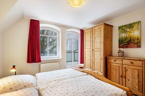 Ein Schlafzimmer mit zwei Betten, einem Holzschrank, einem Fenster mit roten Vorhängen und einem Bild an der Wand.