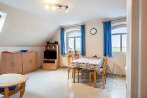 Une pièce comprenant une table à manger, des chaises, un téléviseur, une bibliothèque et une fenêtre avec des rideaux.
