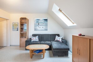 Un salon moderne avec un canapé d’angle gris, un meuble en bois, une table ronde et une lucarne.