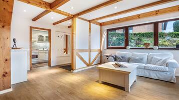 A spacious room with a wooden ceiling, a white sofa, a coffee table, and a view of a garden through large windows.