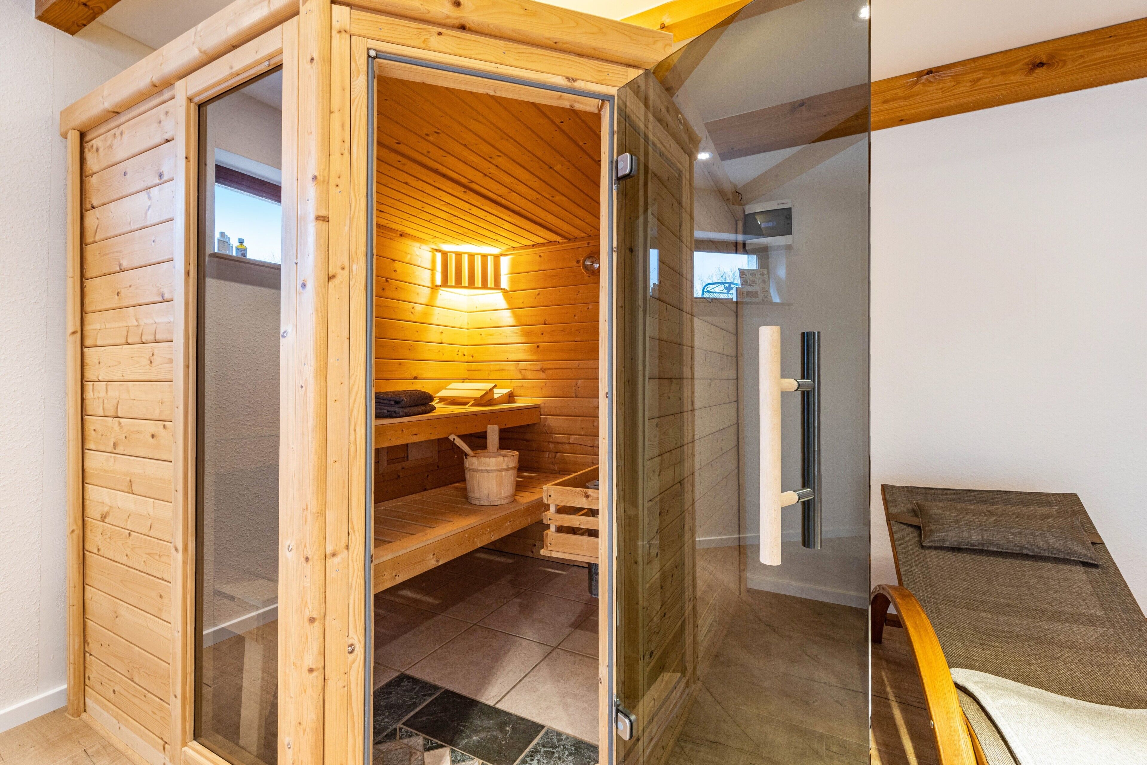 Een houten sauna met een glazen deur, een bank en een handdoekhouder.