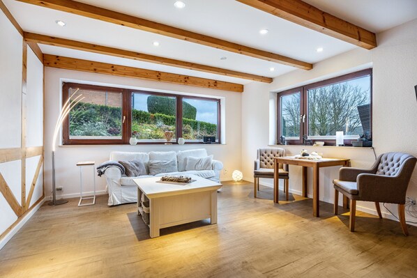 Un'ampia zona giorno con soffitto in legno, ampie finestre, un divano bianco, un tavolino da caffè e un tavolo da pranzo con sedie.