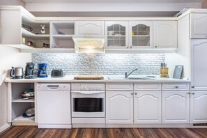 Una cucina compatta con mobili bianchi, lavastoviglie, forno e una parete a mosaico in mattoni.