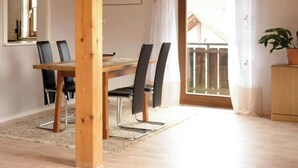 Un comedor con una mesa de madera y cuatro sillas negras, una alfombra, una planta en maceta y vistas a un balcón.