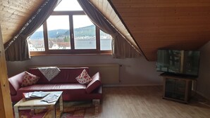 Un acogedor loft con un sofá de cuero rojo, una mesita y un televisor sobre un soporte de madera.